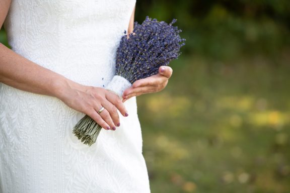 Braut hält ihren Brautstrauß aus eng gebundenem Lavendel auf Bauchhöhe